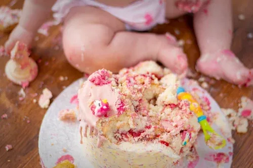 Baby covered in buttercream mid-smash, hands and face full of cake