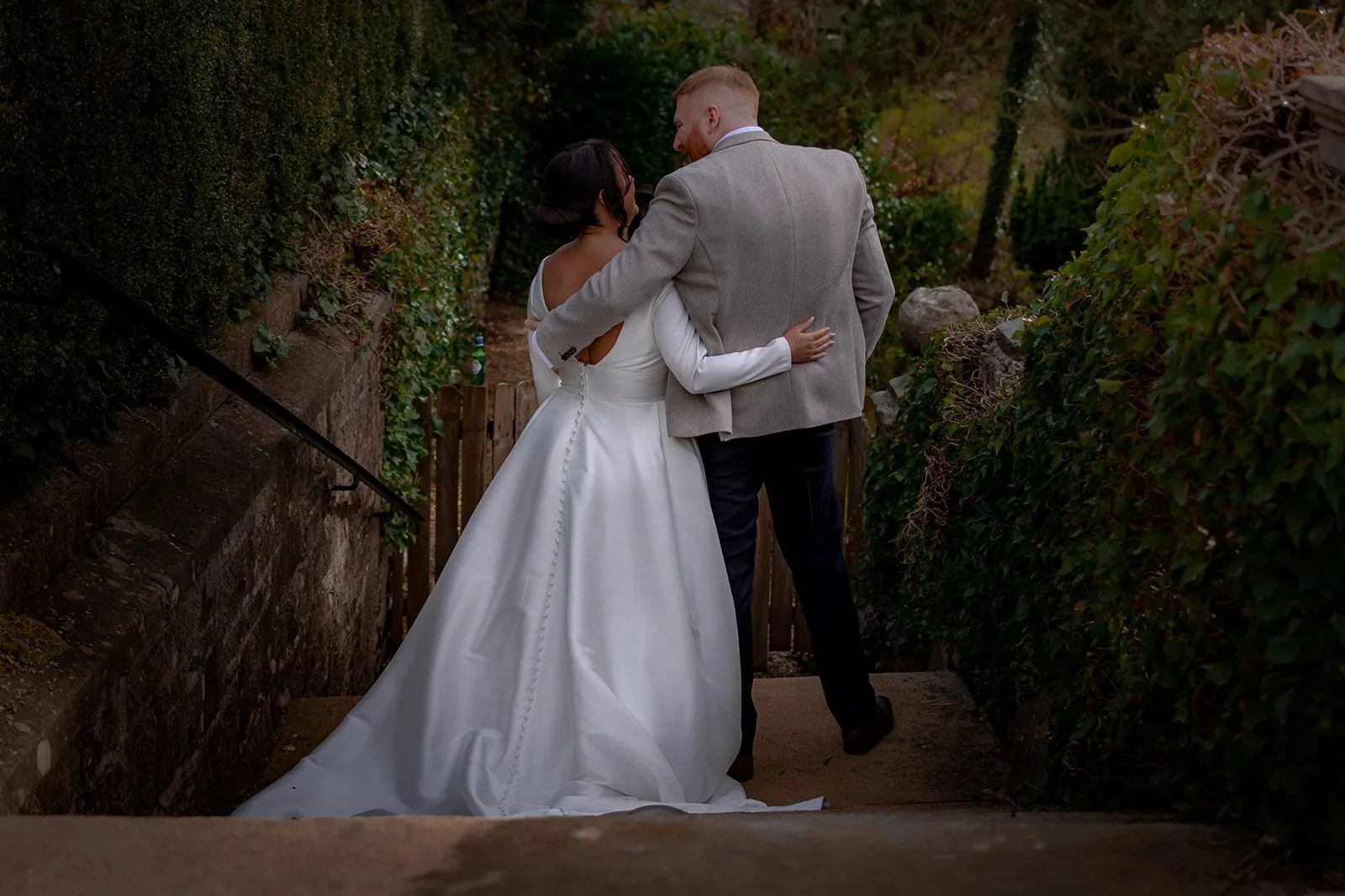 Bride gathering her dress to come down a flight of worn stone garden steps